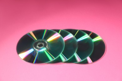 Photo of Many shiny compact discs on pink background, closeup