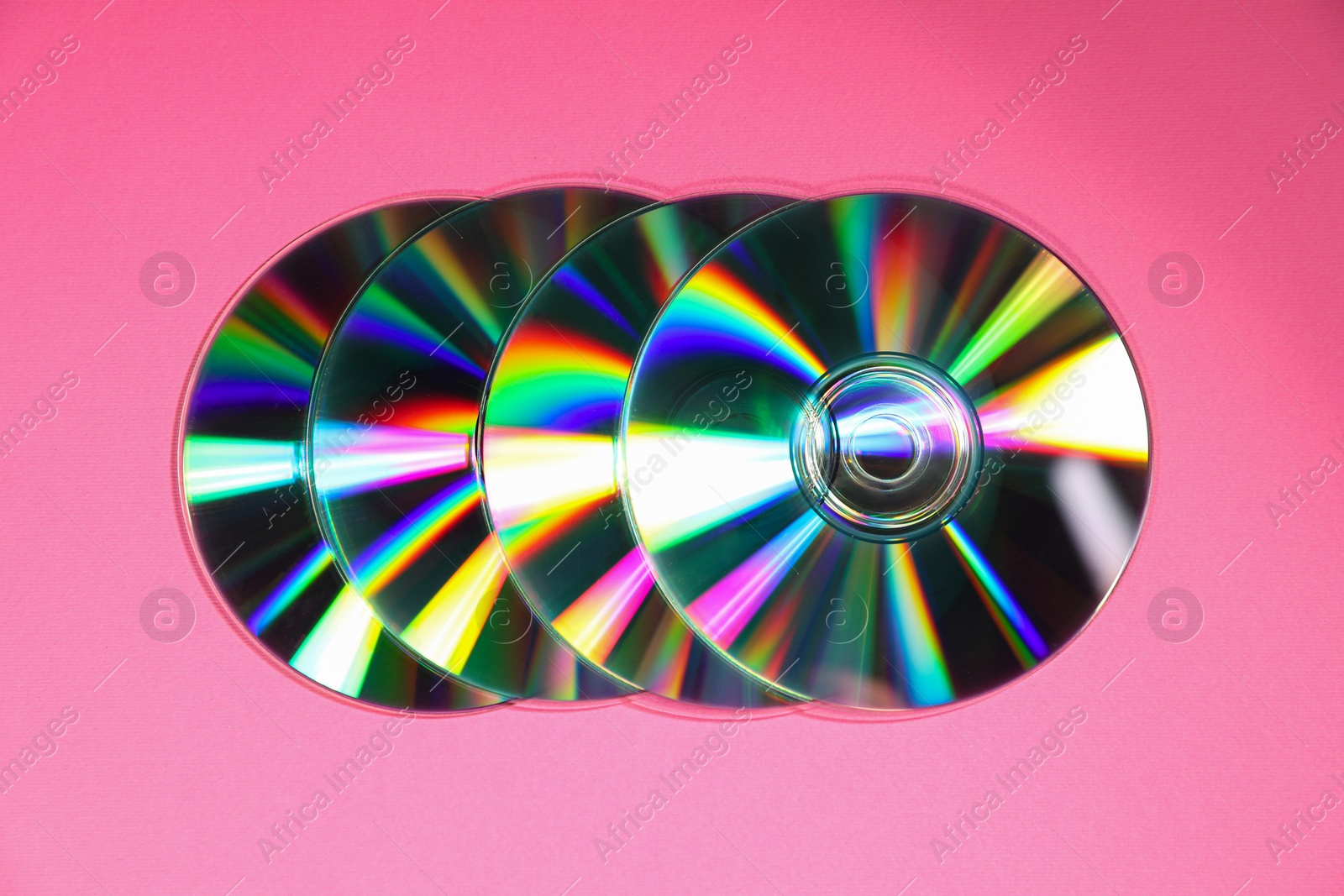 Photo of Many shiny compact discs on pink background, top view