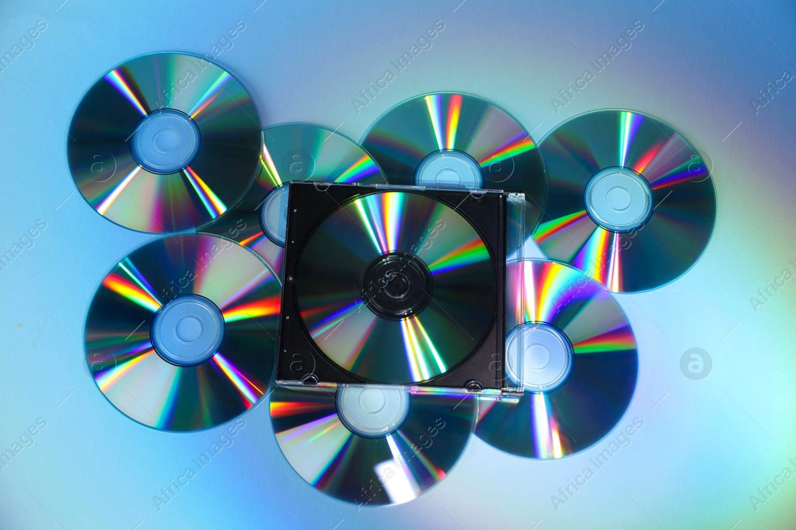 Photo of Many compact discs on light blue background, top view