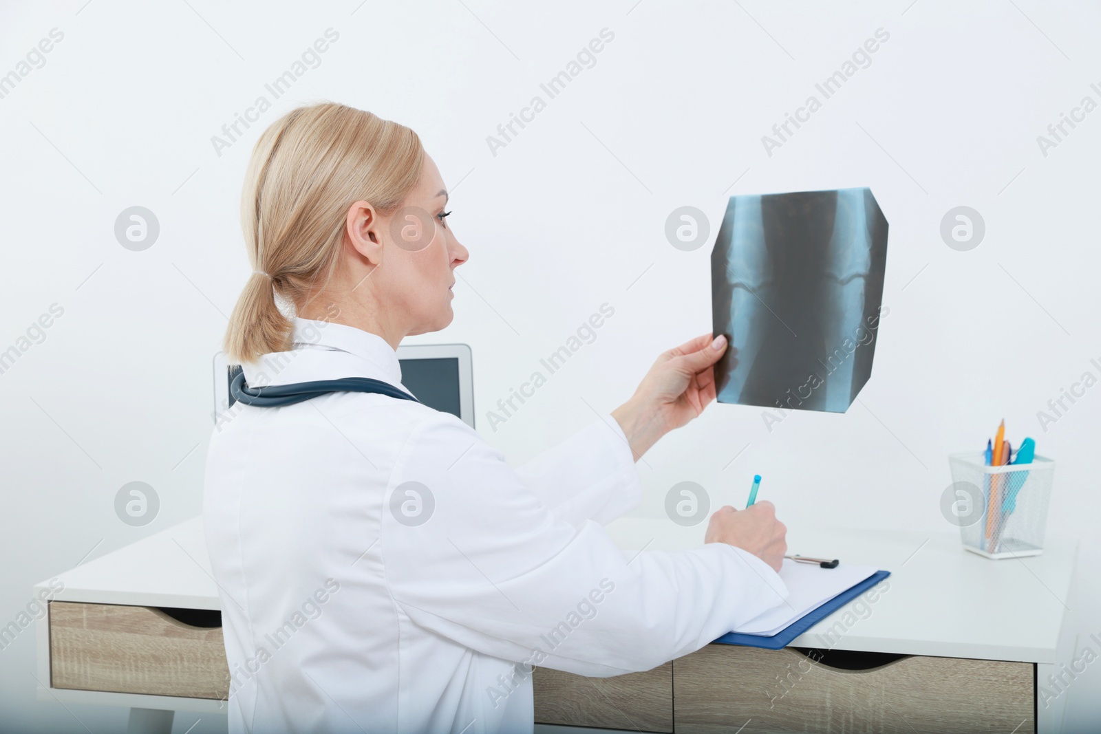 Photo of Doctor examining x-ray image of knee while working at table in clinic