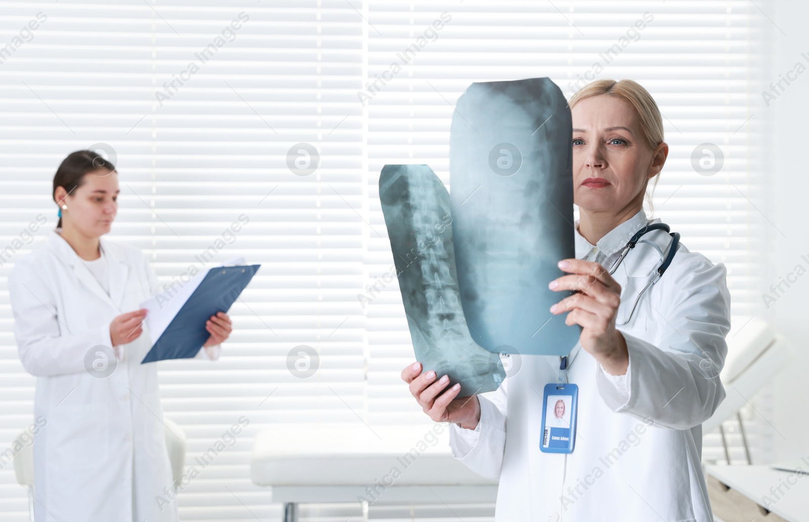 Photo of Doctor examining x-ray images of backbone in clinic. Medical assistant with clipboard indoors