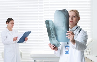 Doctor examining x-ray images of backbone in clinic. Medical assistant with clipboard indoors