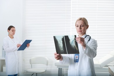 Photo of Doctor examining x-ray image of foot in clinic. Medical assistant with clipboard indoors