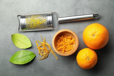 Photo of Orange zest, grater and fresh fruits on gray textured table, flat lay