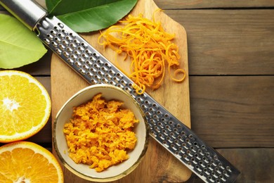 Photo of Orange zest, grater and fresh fruit pieces on wooden table, flat lay. Space for text