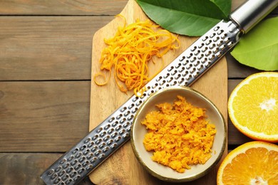 Photo of Orange zest, grater and fresh fruit pieces on wooden table, flat lay. Space for text