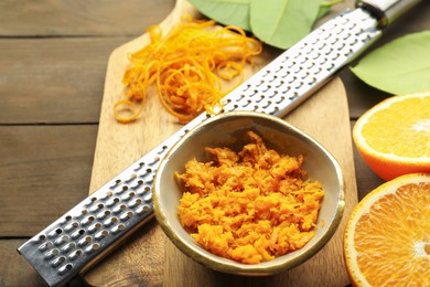 Photo of Orange zest, grater and fresh fruit pieces on wooden table, closeup