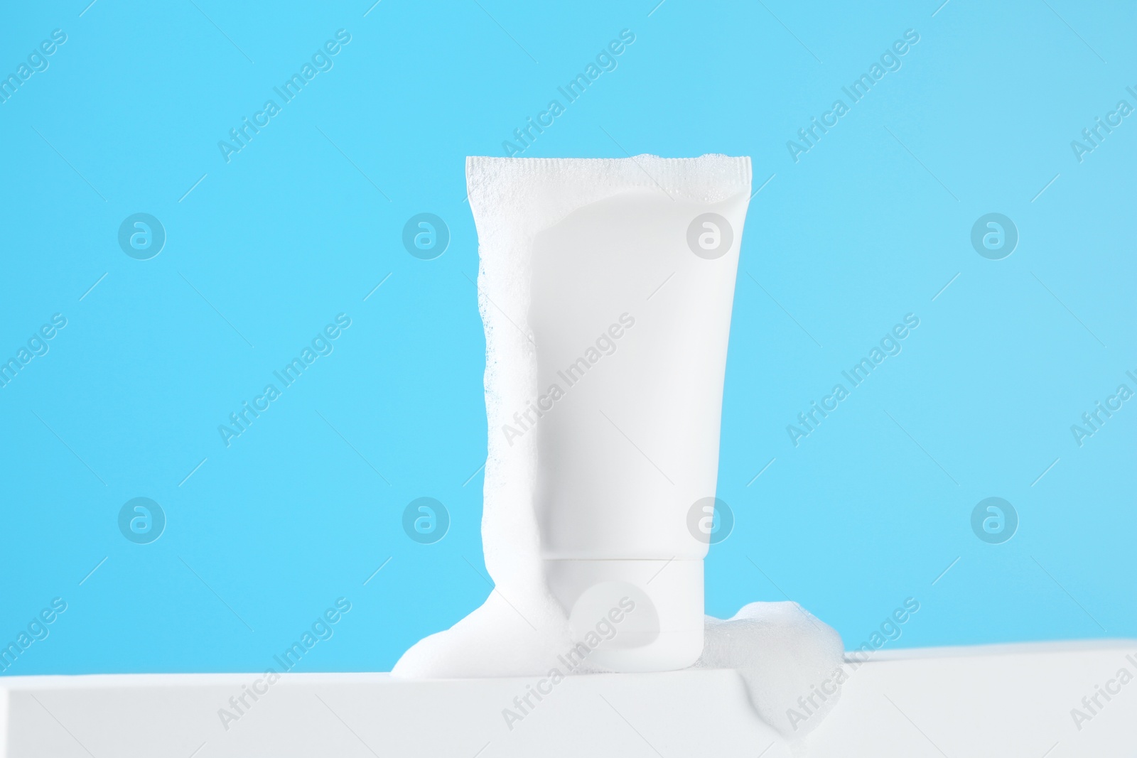 Photo of Tube of cosmetic product with foam on podium against light blue background