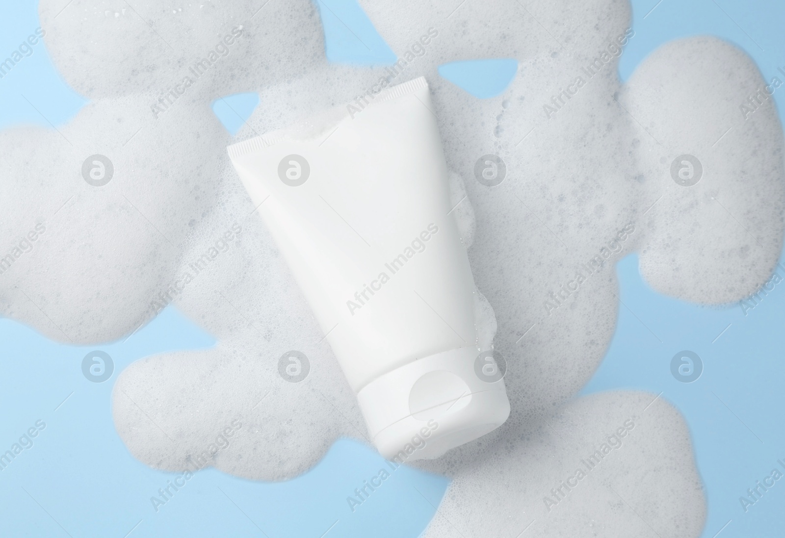 Photo of Tube of cosmetic product with foam on light blue background, top view