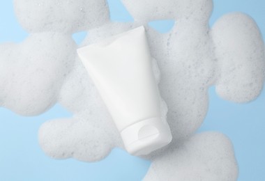 Photo of Tube of cosmetic product with foam on light blue background, top view