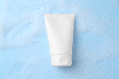 Tube of cosmetic product with foam on light blue background, top view