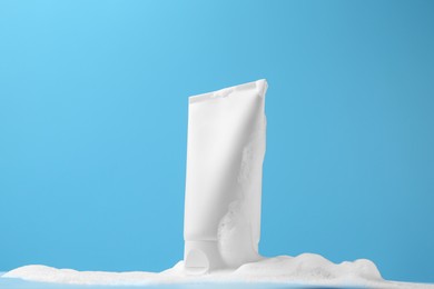 Photo of Tube of cosmetic product with foam on light blue background