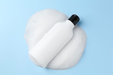 Bottle of cosmetic product with foam on light blue background, top view