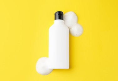 Bottle of cosmetic product with foam on yellow background, top view