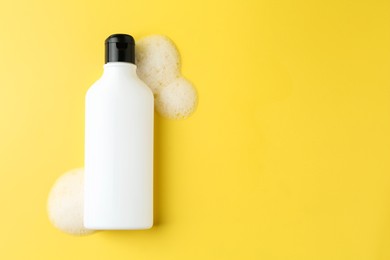 Photo of Bottle of cosmetic product with foam on yellow background, top view. Space for text