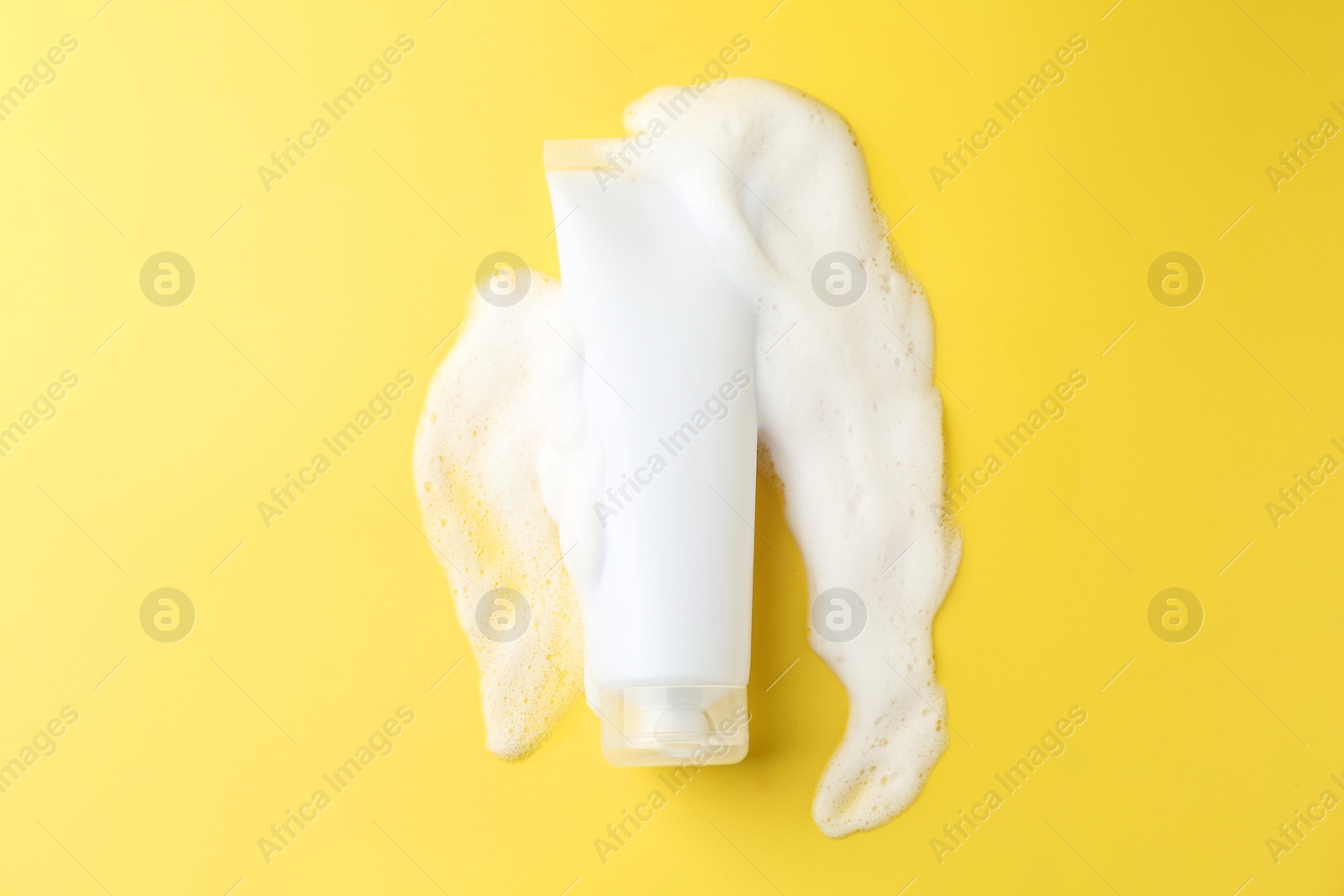 Photo of Tube of cosmetic product with foam on yellow background, top view