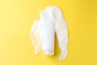 Photo of Tube of cosmetic product with foam on yellow background, top view