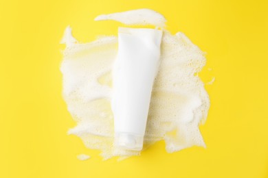 Photo of Tube of cosmetic product with foam on yellow background, top view