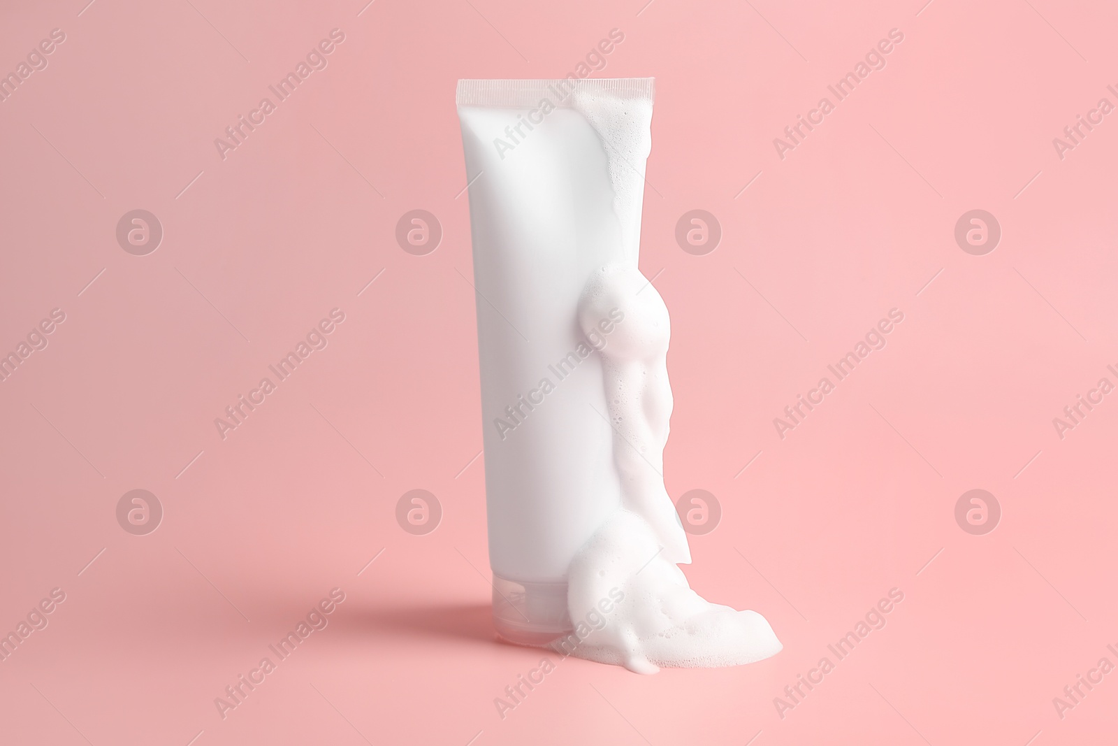 Photo of Tube of cosmetic product with foam on pink background