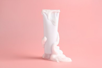 Photo of Tube of cosmetic product with foam on pink background