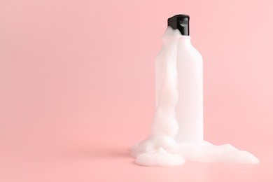 Photo of Bottle of cosmetic product with foam on pink background, space for text