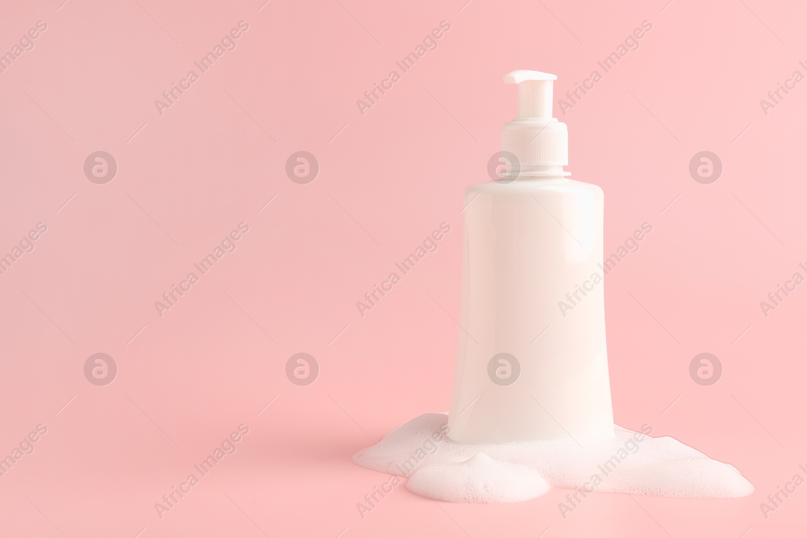 Photo of Bottle of cosmetic product with foam on pink background, space for text