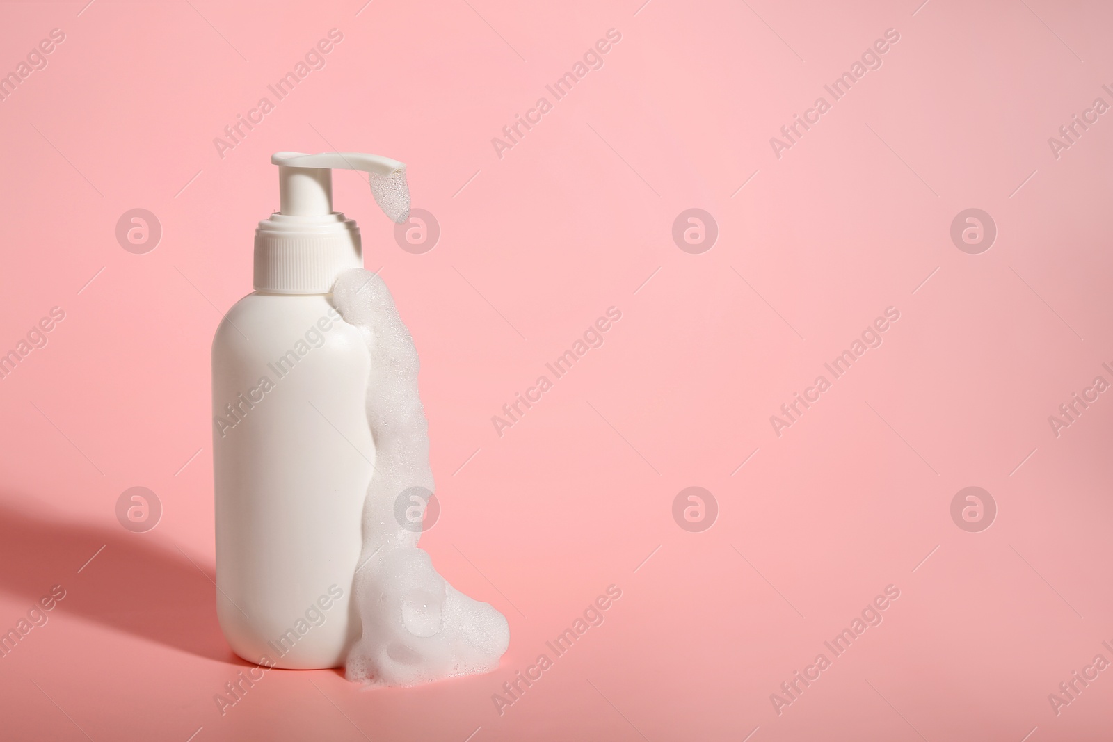 Photo of Bottle of cosmetic product with foam on pink background, space for text