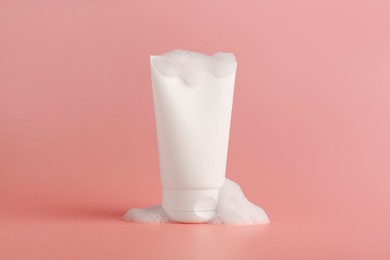 Tube of cosmetic product with foam on pink background