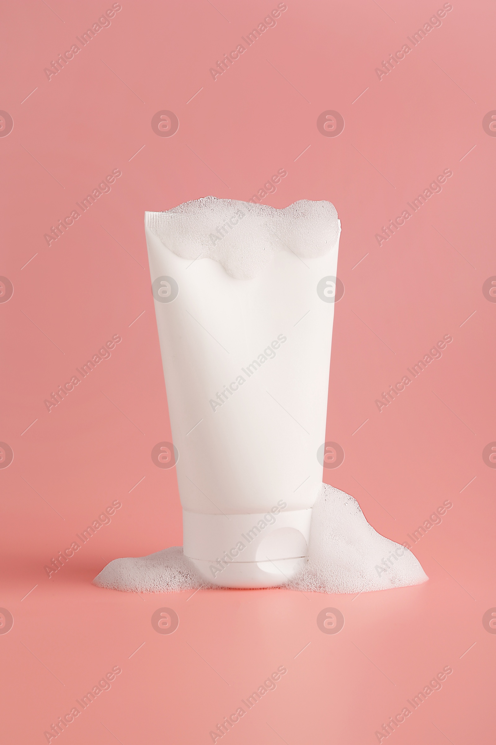 Tube of cosmetic product with foam on pink background Photo of Tube of cosmetic product with foam on pink background