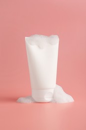 Photo of Tube of cosmetic product with foam on pink background