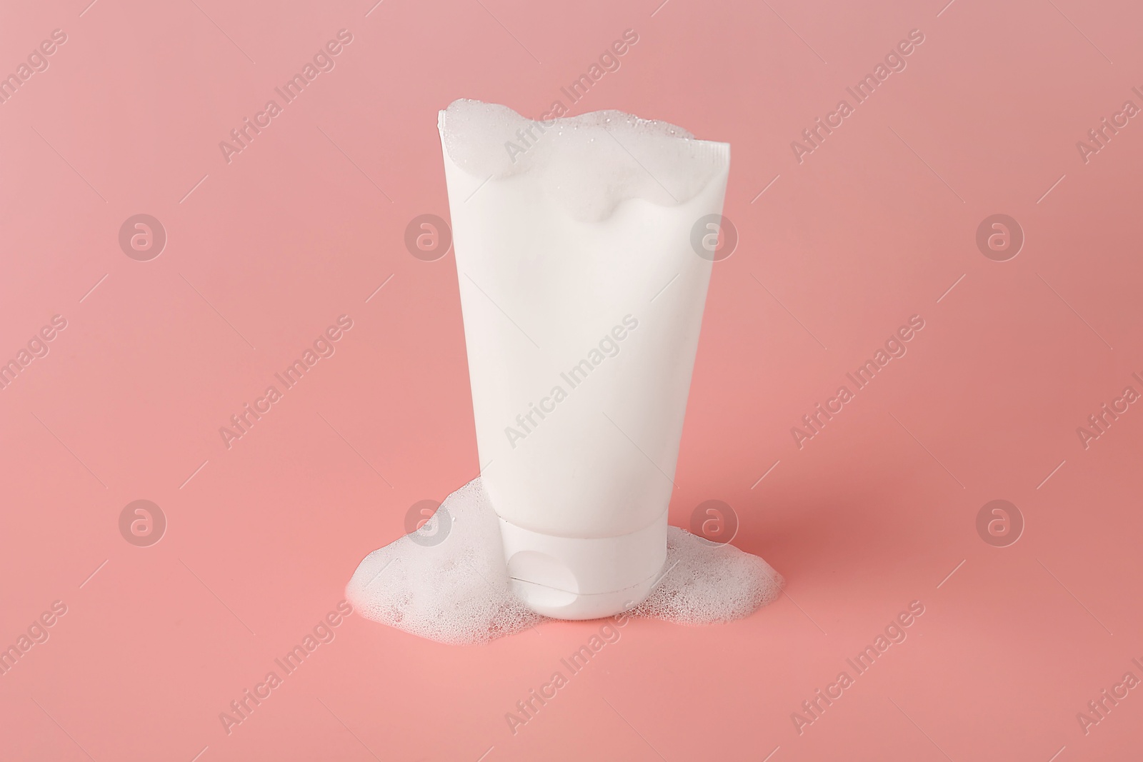 Photo of Tube of cosmetic product with foam on pink background