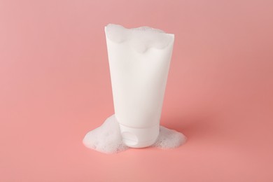 Tube of cosmetic product with foam on pink background