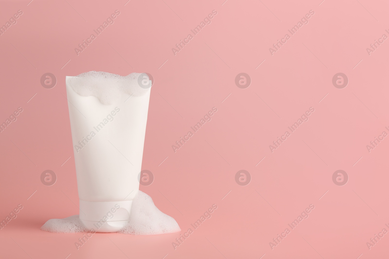 Photo of Tube of cosmetic product with foam on pink background, space for text