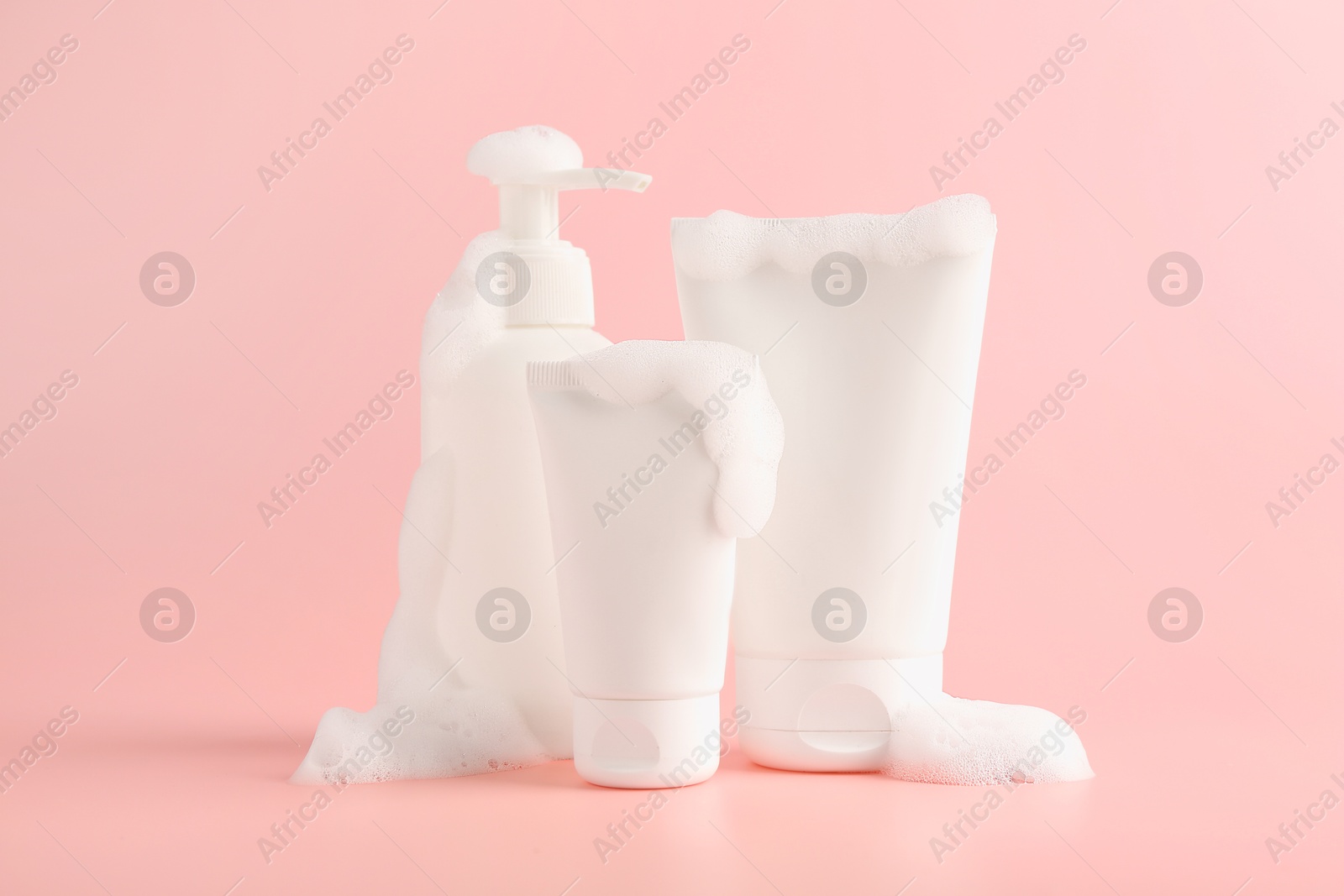 Photo of Tubes and bottle of cosmetic products with foam on pink background