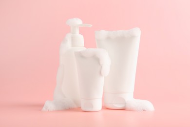 Photo of Tubes and bottle of cosmetic products with foam on pink background