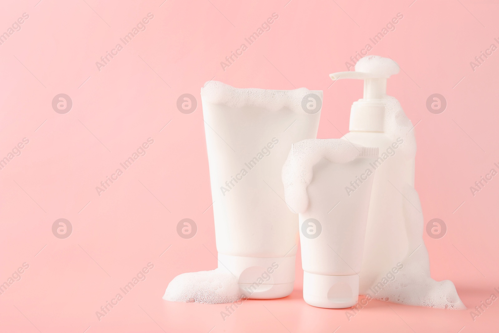 Photo of Tubes and bottle of cosmetic products with foam on pink background, space for text