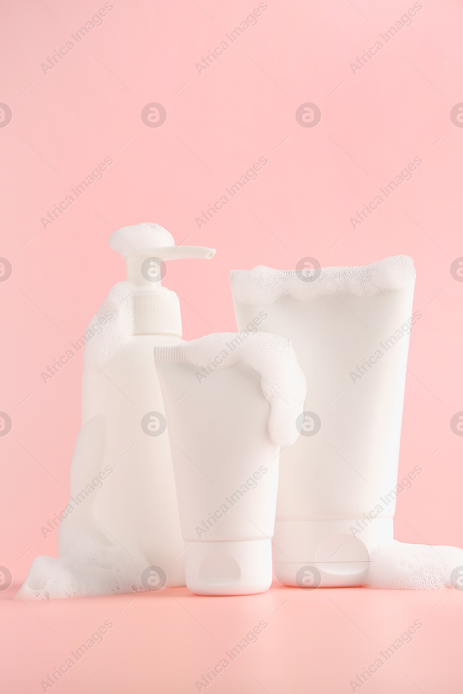 Photo of Tubes and bottle of cosmetic products with foam on pink background