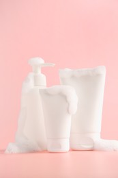 Photo of Tubes and bottle of cosmetic products with foam on pink background