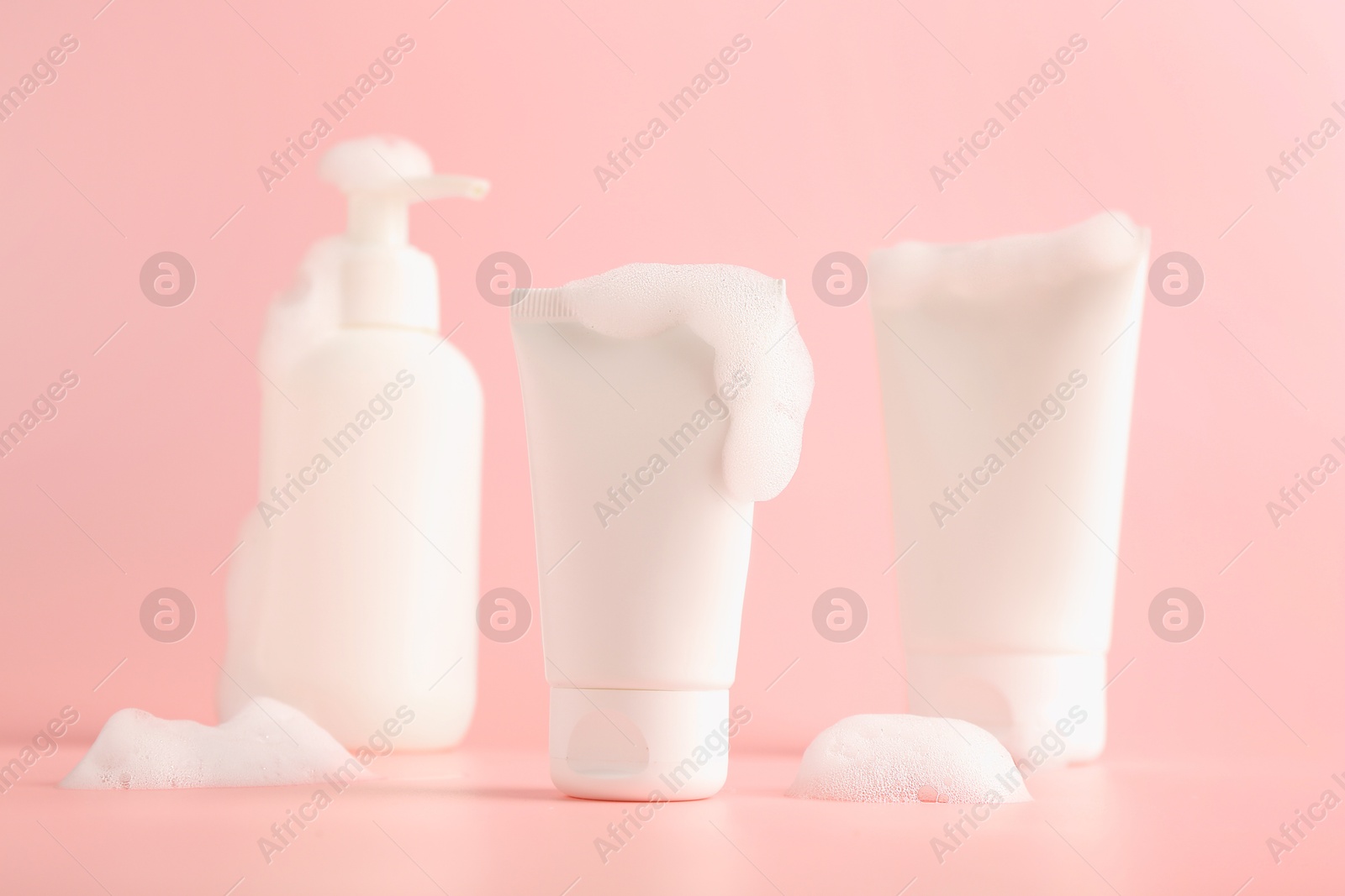 Photo of Tubes and bottle of cosmetic products with foam on pink background