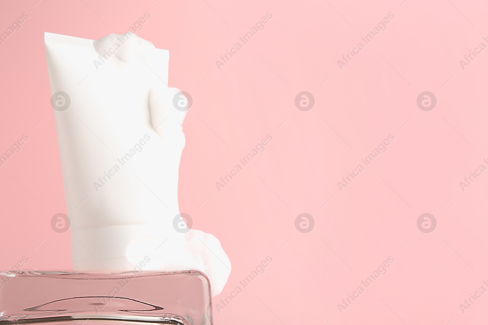 Photo of Tube of cosmetic product with foam on pink background, space for text