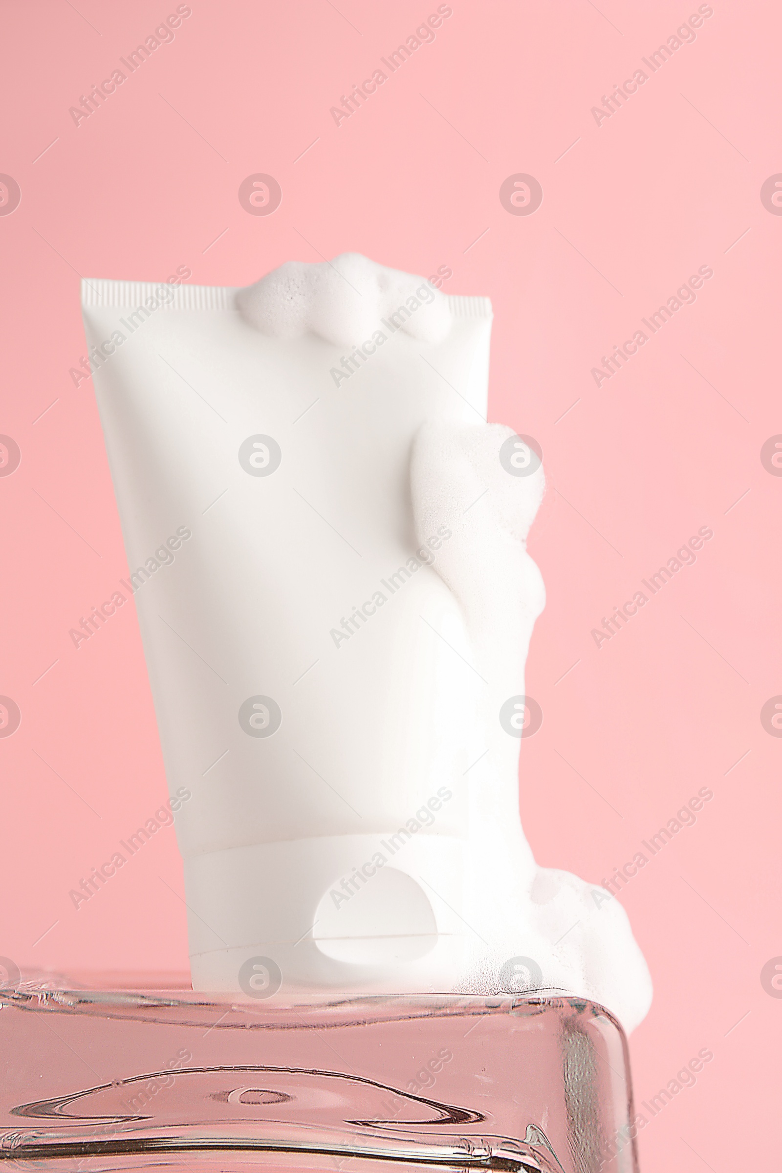 Photo of Tube of cosmetic product with foam on pink background, closeup