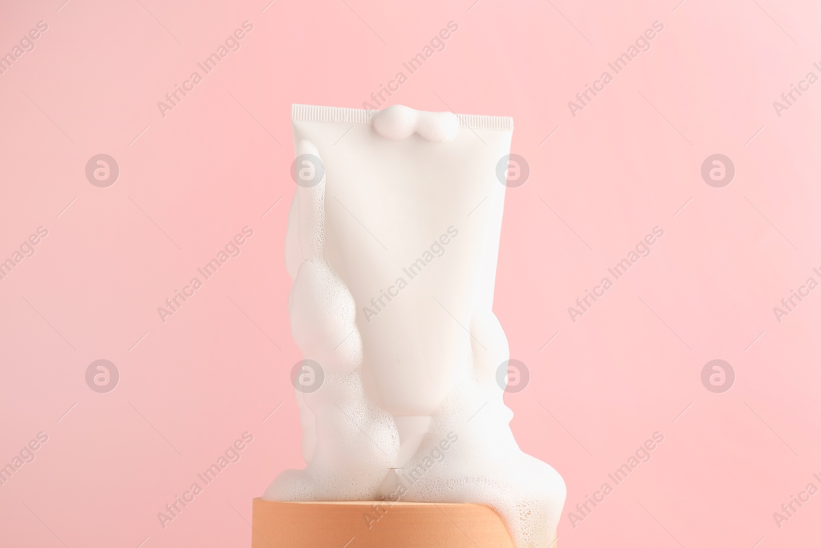 Photo of Tube of cosmetic product with foam on podium against pink background