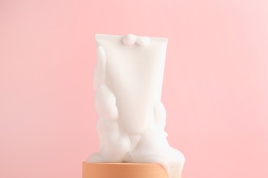 Tube of cosmetic product with foam on podium against pink background