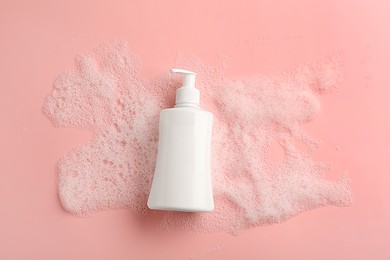 Photo of Bottle of cosmetic product with foam on pink background, top view