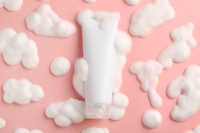 Tube of cosmetic product with foam on pink background, top view