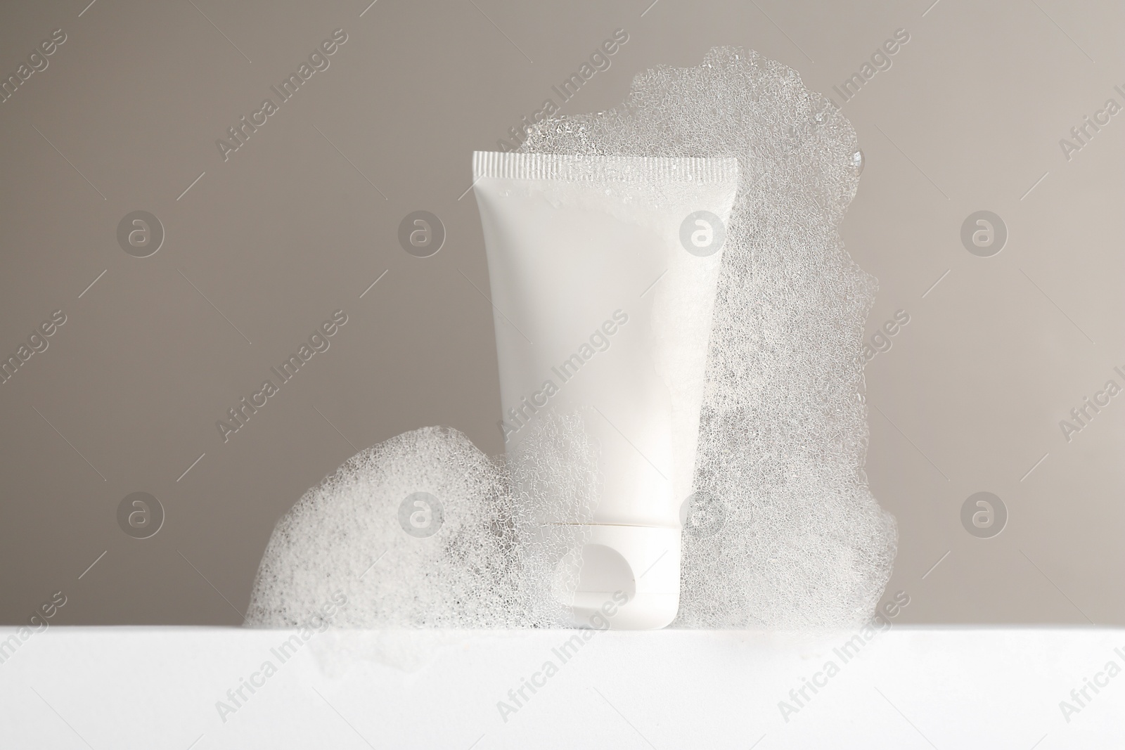 Photo of Tube of cosmetic product with foam on white surface against grey background