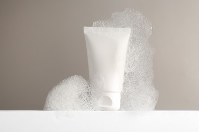 Photo of Tube of cosmetic product with foam on white surface against grey background