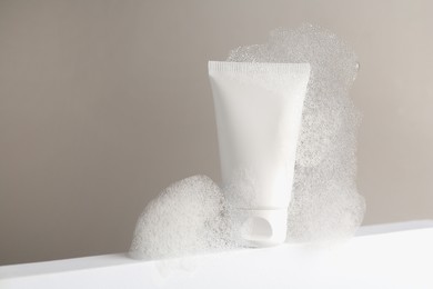 Photo of Tube of cosmetic product with foam on white surface against grey background