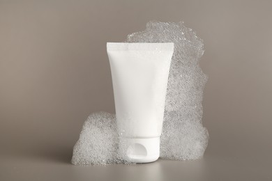 Photo of Tube of cosmetic product with foam on grey background