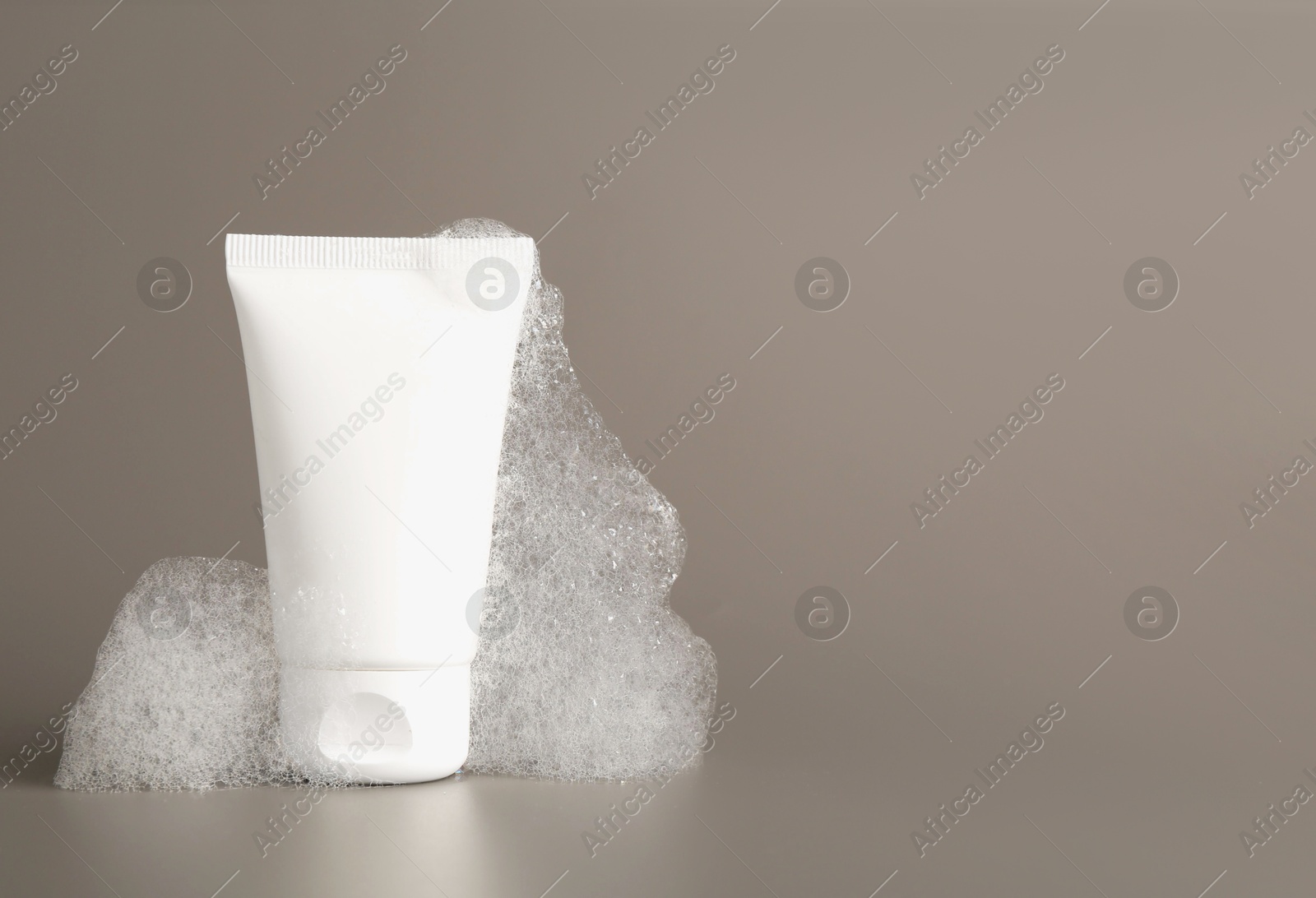 Photo of Tube of cosmetic product with foam on grey background, space for text